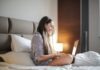 The Latest Online Dating Security Tips Side View Photo of Smiling Woman in a Black and White Striped Top Sitting on a Bed While Using a Laptop