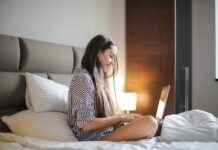 The Latest Online Dating Security Tips Side View Photo of Smiling Woman in a Black and White Striped Top Sitting on a Bed While Using a Laptop